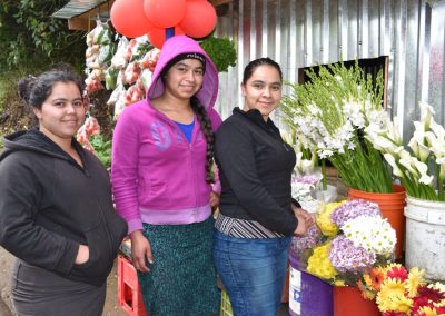 three women smiling next to bins of flowers.