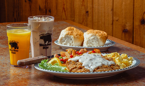 Chicken Fried Steak with a side of biscuits. Shown with OJ and a cold brew coffee